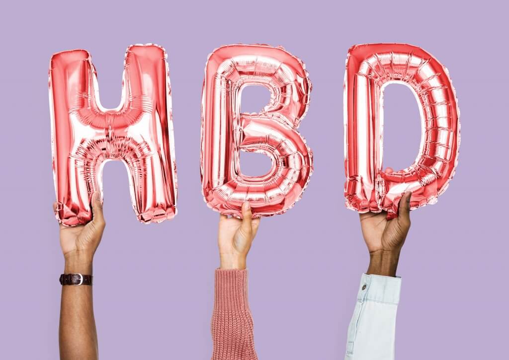 Three hands holding metallic “HBD” balloons 